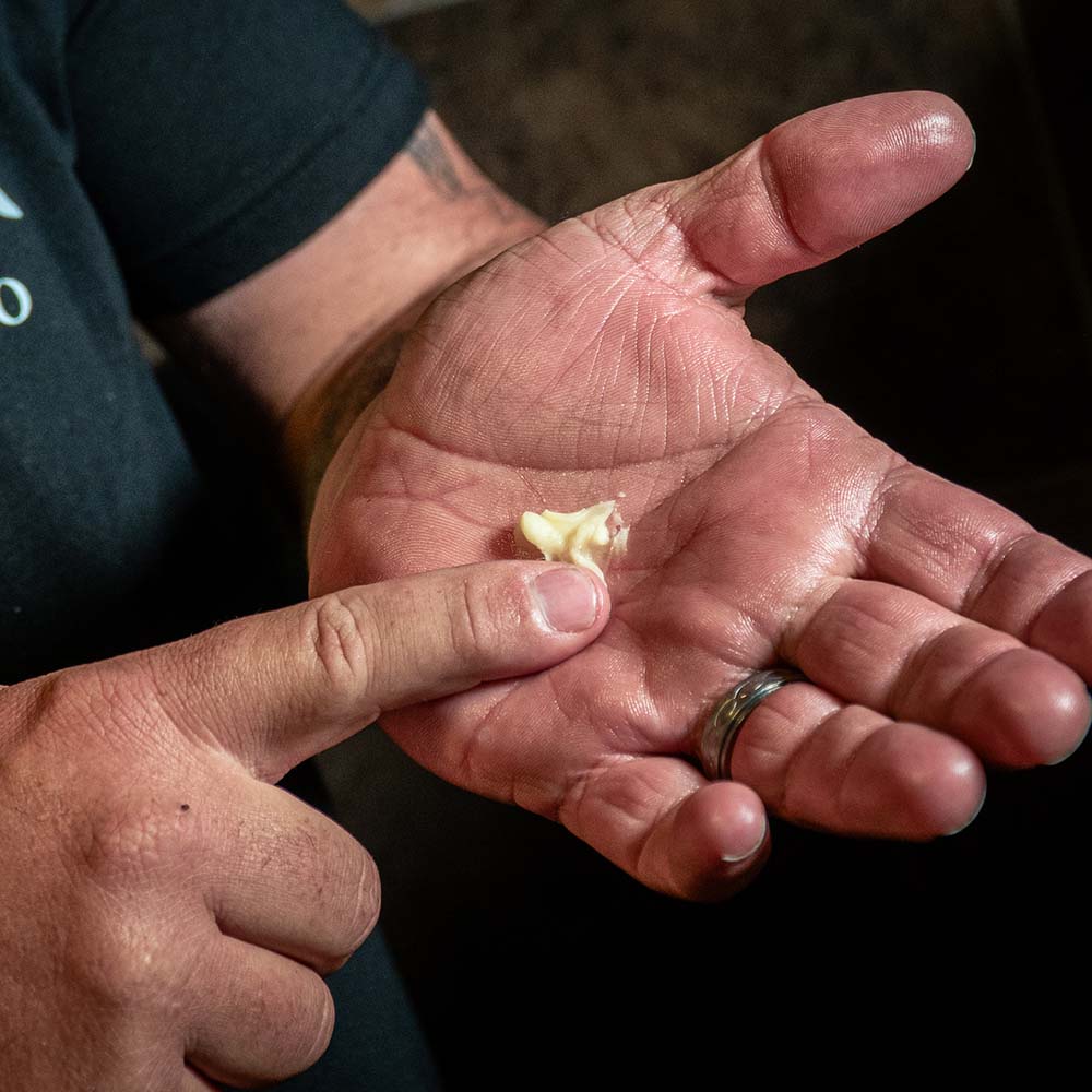 A man's finger applying beard butter onto the palm of his hand