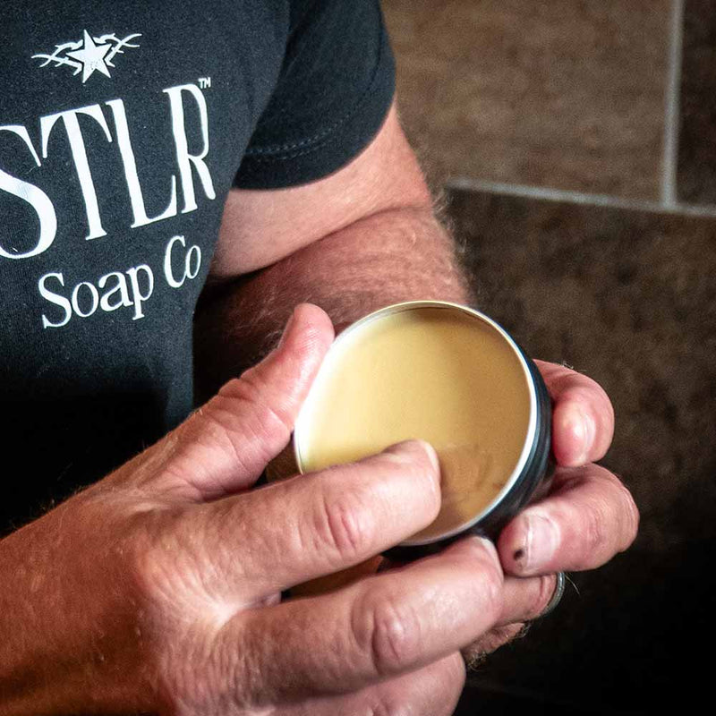a man's hand scooping beard butter from its container