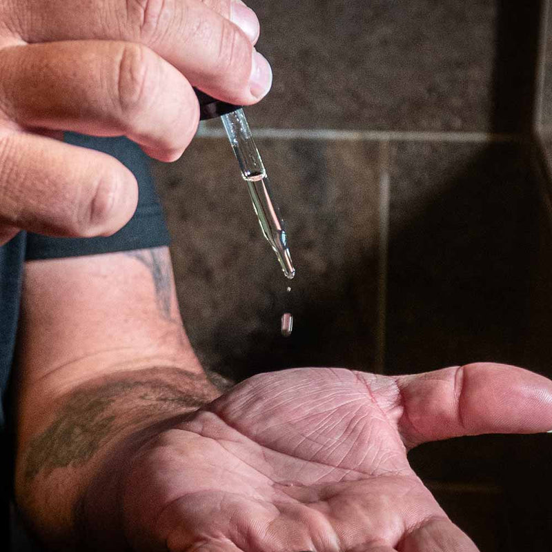 beard oil falling from a dropper onto the palm of a man's hand