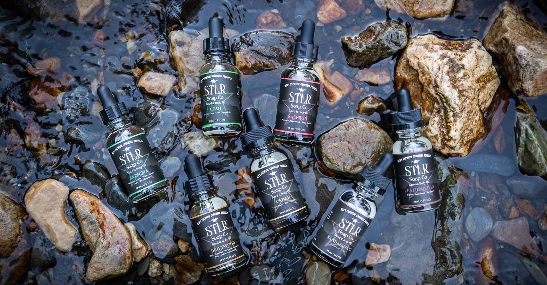 Collection of beard oils in a stream of water surrounded by rocks