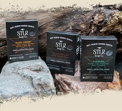 three packaged soaps resting on rocks in nature setting with overlayed grunge borders for mobile devices